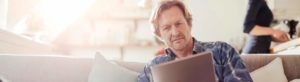 A man sits on a sofa and reads about buy to let mortgages on his tablet