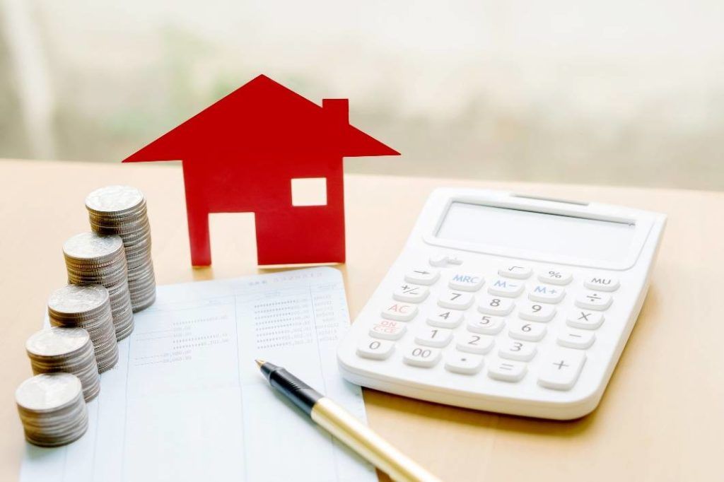 Small stacks of money on a desk with a red house, pen, bank statement and calculator