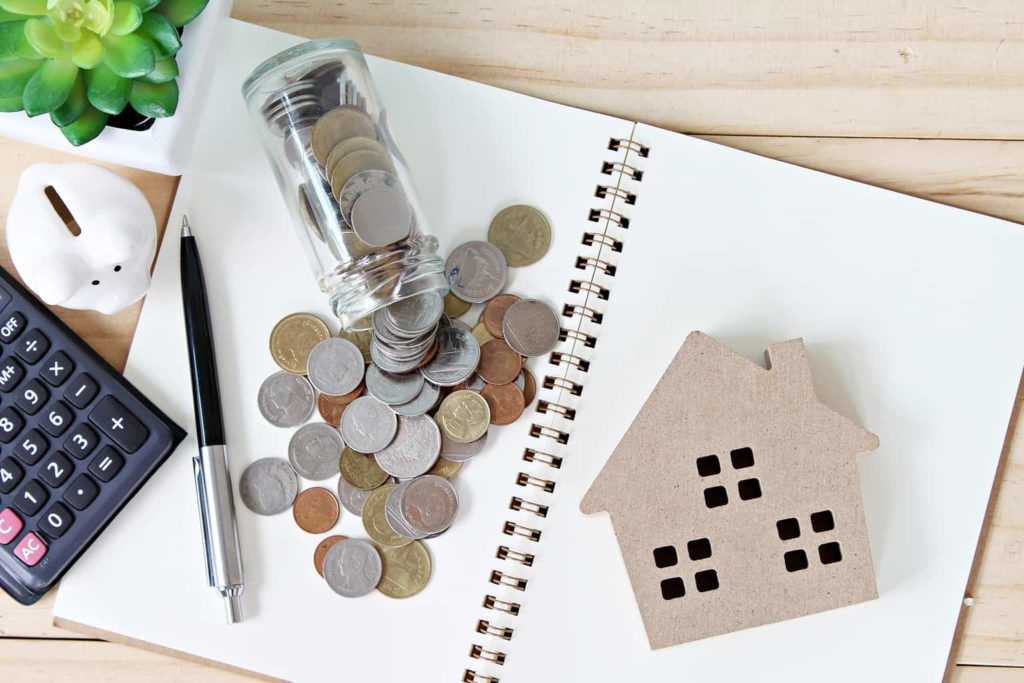 An open notepad with a coin jar spilled across it along with a house shaped coaster, a pen and calculator as the owner considers a remortgage