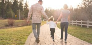 A man and woman hold the hands of their child and walk along a path after buying life insurance