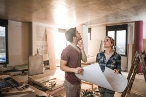 Young thoughtful couple with blueprints inside of renovating apartment.