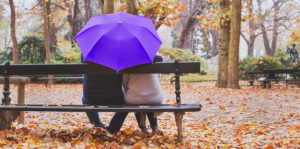 elderly retired couple sitting together under umbrella