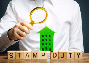 Businessman puts wooden blocks with the word Stamp duty and house. Taxes assessed during the transfer of real estate between two parties. Buying housing and land. Property. Stamp Duty Land Tax/ SDLT