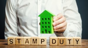 Businessman and wooden blocks with the word Stamp duty and house. Taxes assessed during the transfer of real estate between two parties. Buying housing and land. Property. Stamp Duty Land Tax/ SDLT