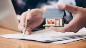 Close up real estate agent with house model hand putting signing contract,have a contract in place to protect it,signing of modest agreements form in office.Concept real estate,moving home or renting property